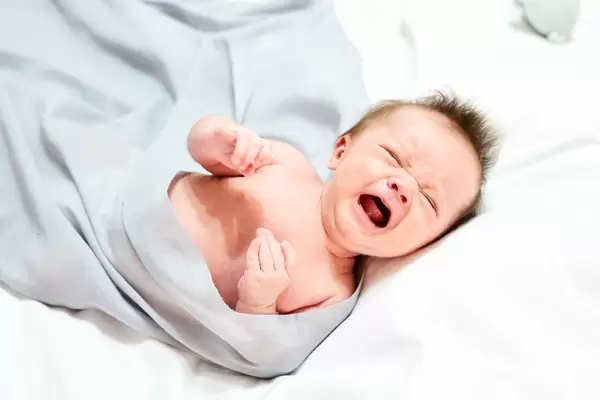 A 1-month crying baby boy on the bed - concept of baby feeling expression in the first year