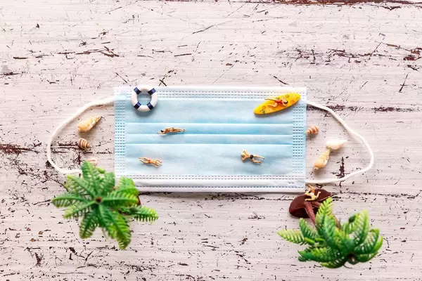 A beach made of a face mask with miniature figures swimming on it. Protection from the coronavirus