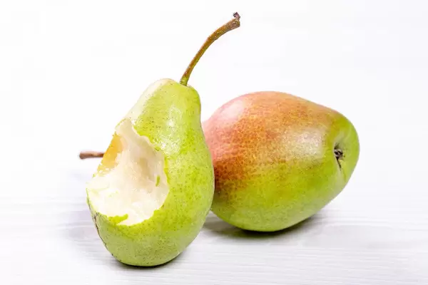 A bitten pear and a whole pear on a white wooden background