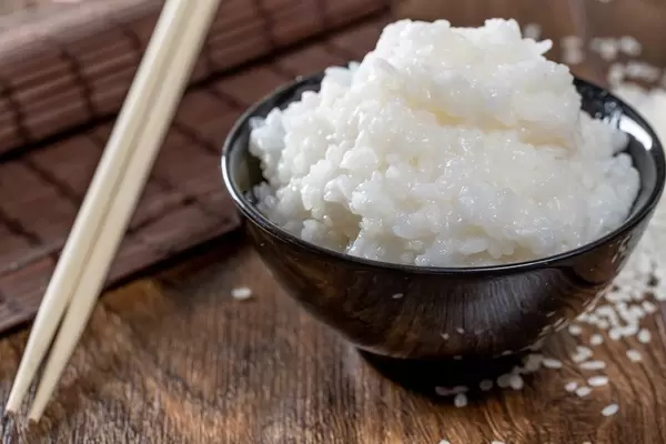 A black bowl of rice with bamboo placemat and chopsticks