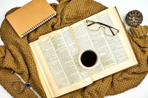 A book and cup of black coffee on a knitted brown sweater