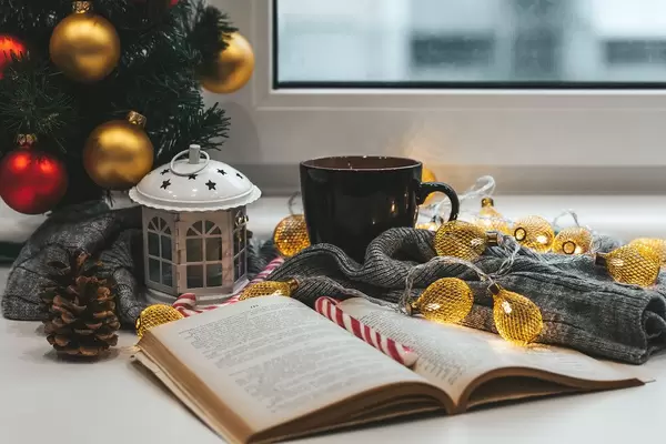 A book with a Christmas tree, a cup of tea and garlands on a background of a window. Winter home relaxation concept (Flip 2019)