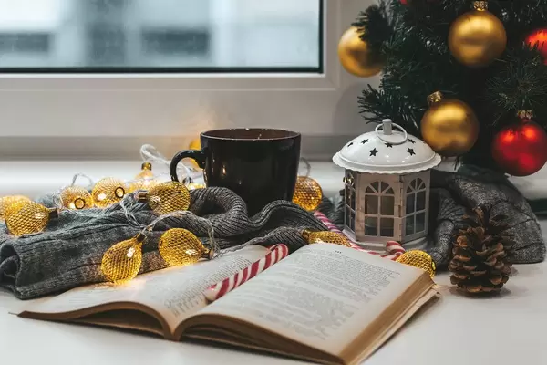 A book with a Christmas tree, a cup of tea and garlands on a background of a window. Winter home relaxation concept