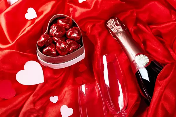 A bottle of champagne with glasses and sweets on a red silk fabric
