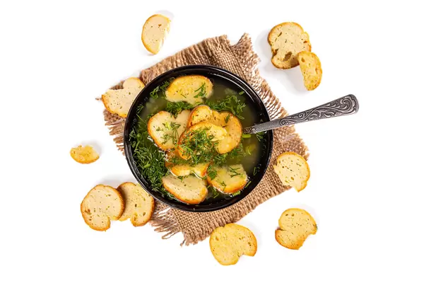 A bowl of soup with croutons and dill on a white background, top view