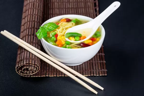 A bowl of vegetable soup with macaroni on a black background