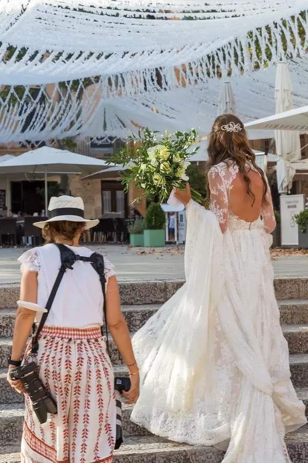 A bride in a long white dress with open back walking up stairs with her photographer, seen from behind