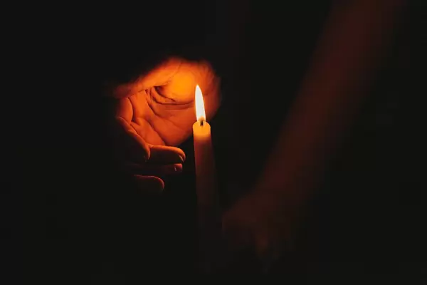 A burning candle at night, protected by the hand of a woman