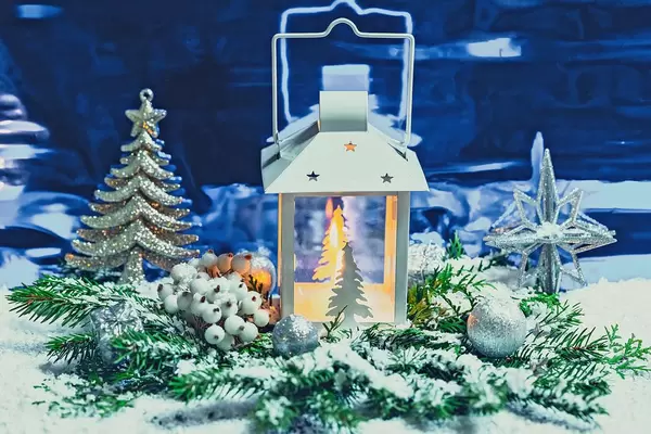 A Christmas lanternis shining on a blue background with branches of a Christmas tree, decor and snow. The concept of magical holidays