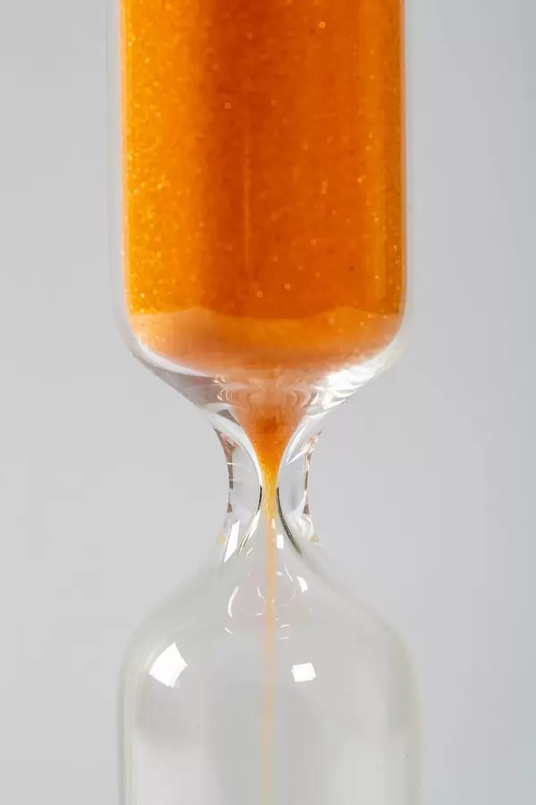 A closeup of an hourglass with falling sand on a white background