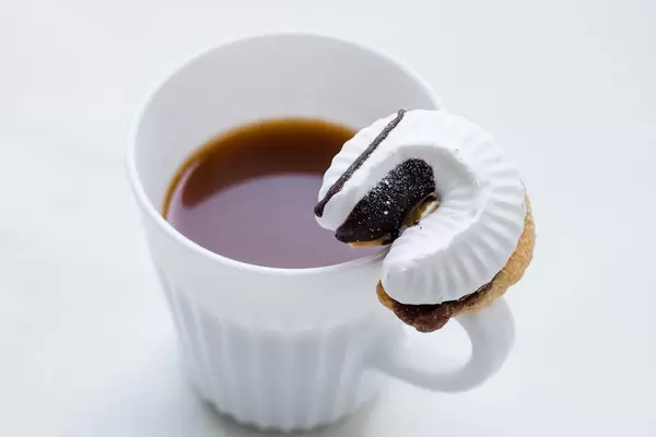 A cup of coffee and a cookie with a cream