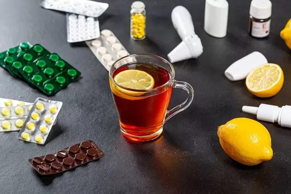 A Cup of hot tea with fresh lemon on a black background with a bunch of drugs