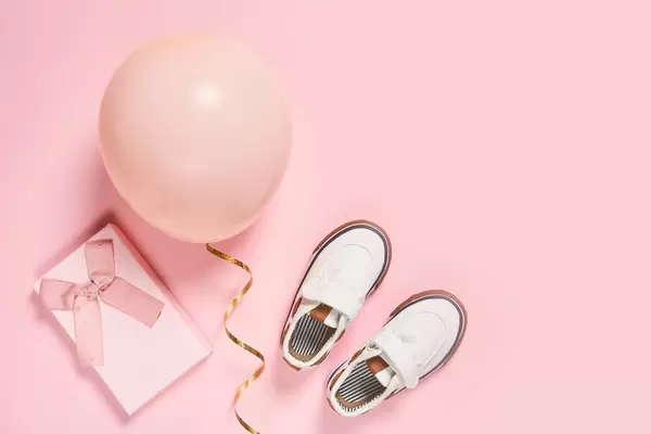 A cute gift box, baby booties and balloon on bright pink background