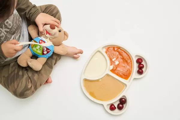 A cute little kid feeding his toy bear