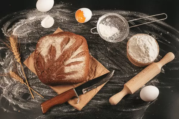 A delicious rye bread on the table with flour, eggs and wheat spikelets, top view