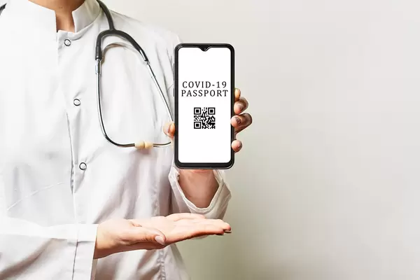 A doctor in a white medical suite with a stethoscope holding up a smartphone with COVID-19 Immune ID app