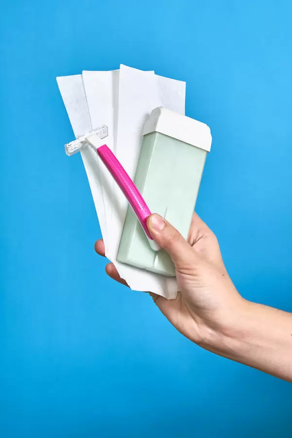 A female hand holds hair removal accessories - waxing tools and razor shaver