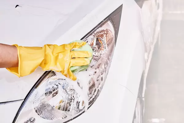 A female person in rubber gloves scrubbing vehicle front lights