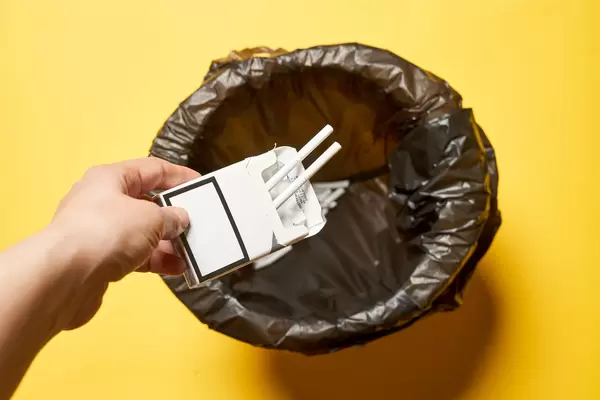 A female throwing cigarettes pocket into the garbage can - concept of quitting smoking