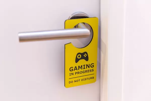 A gamer's room: white door with yellow "Gaming in progress - do not disturb" sign hanging from the door handle