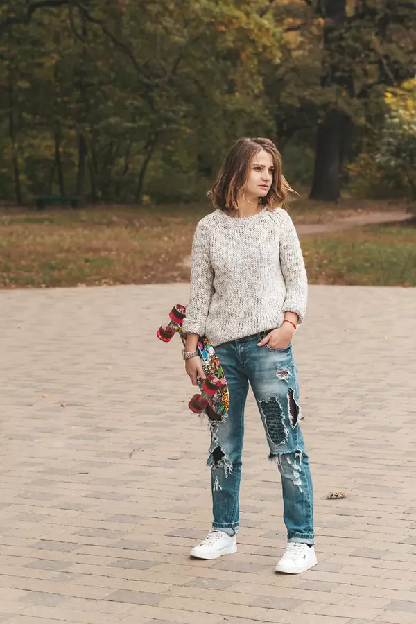 A girl in an autumn park holds a skate in her hand
