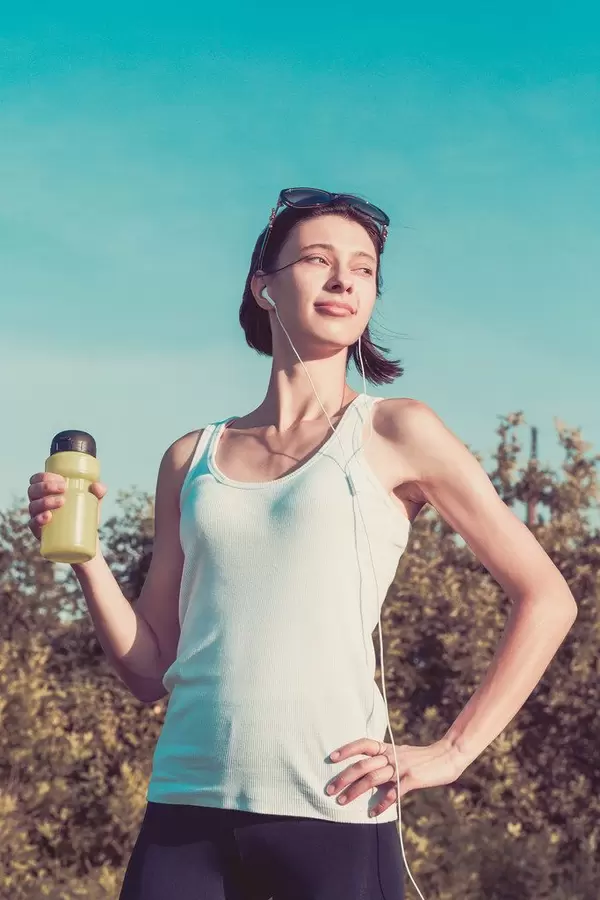A girl in sports clothes with headphones and a bottle of water in nature. The concept of sports