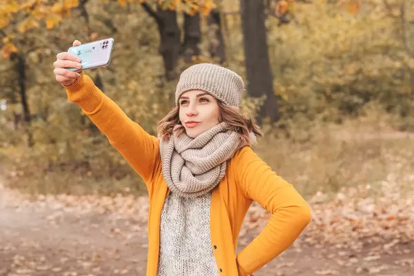 A girl is photographed in an autumn park on her mobile