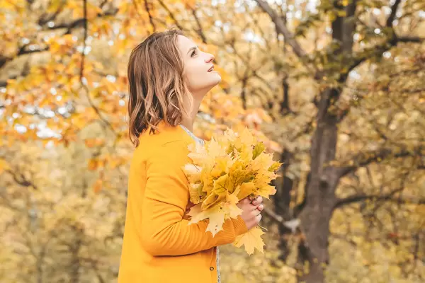 A girl looks at an autumn Park with leaves in her hands