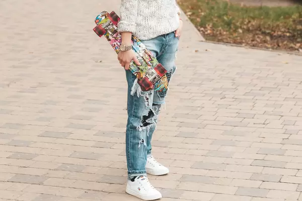 A girl with a skateboard in her hand stands on the street