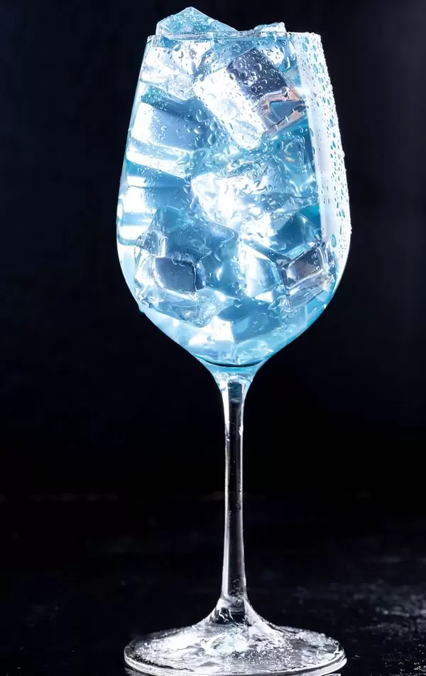 A glass filled with a blue cocktail with ice on black background (Flip 2019)