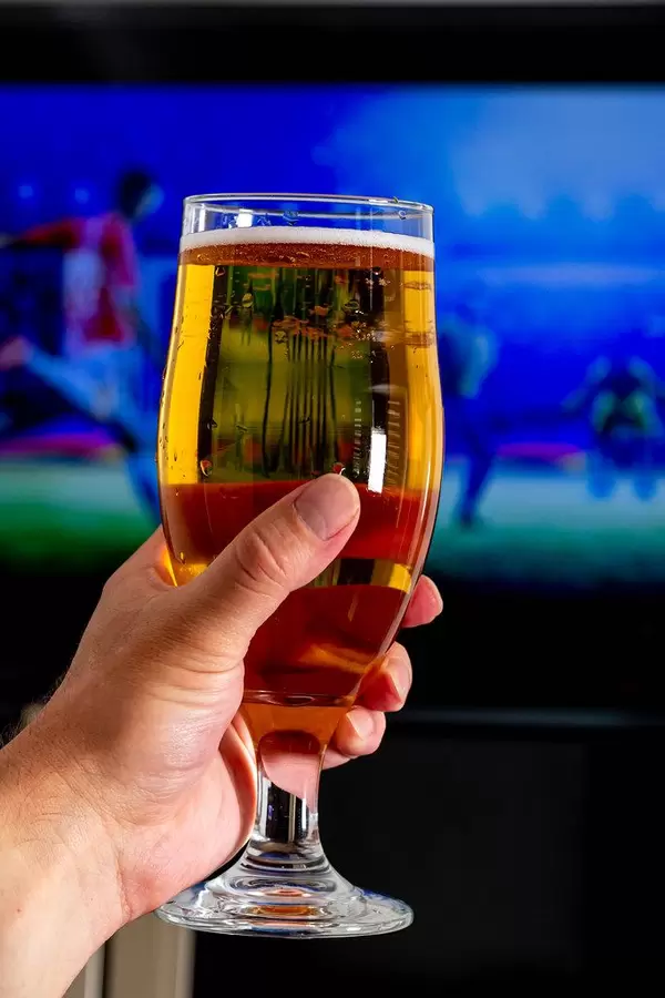 A glass in a man's hand against the background of the television screen with football. Fan concept