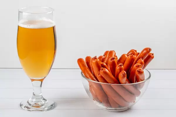 A glass of beer and smoked sausages in a bowl