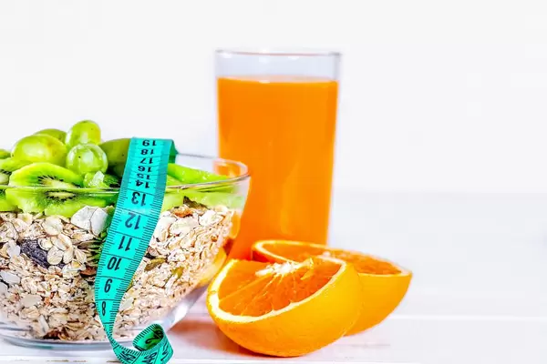 A glass of freshly squeezed orange juice and measuring tape on the plate cereal porridge with kiwi slices. Diet food