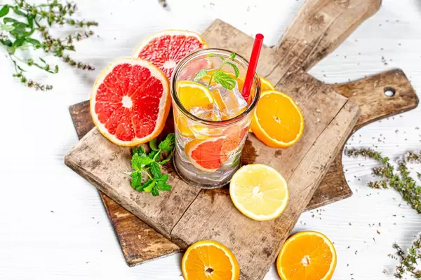 A glass of lemonade with ice cubes, sliced citrus and mint on old wooden boards