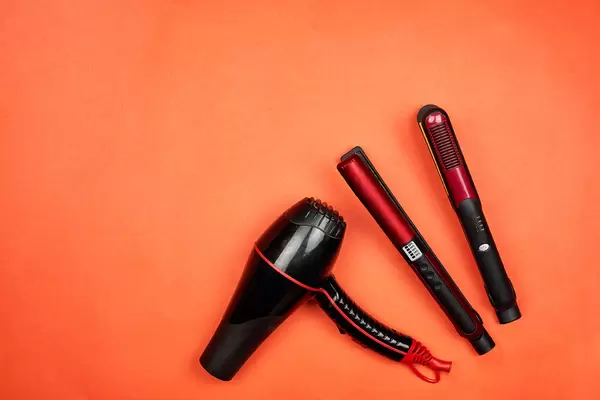 A hairdryer and hair straightening iron on red background