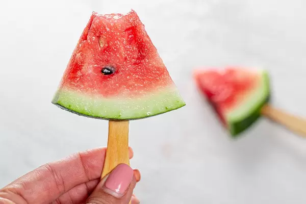 A half-eaten slice of ripe watermelon on a stick