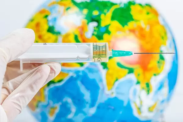 A hand in a glove holds a syringe on a background of the globe. Health protection concept