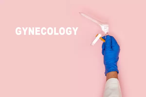 A hand of gynecologist holding vaginal speculum over pink background