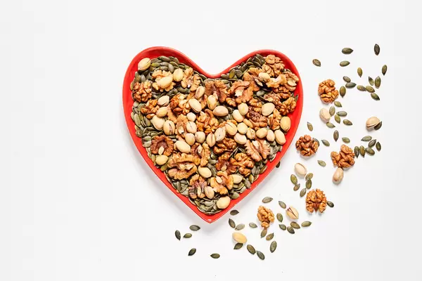 A heart-shaped plate full with various types of nuts on white backdrop
