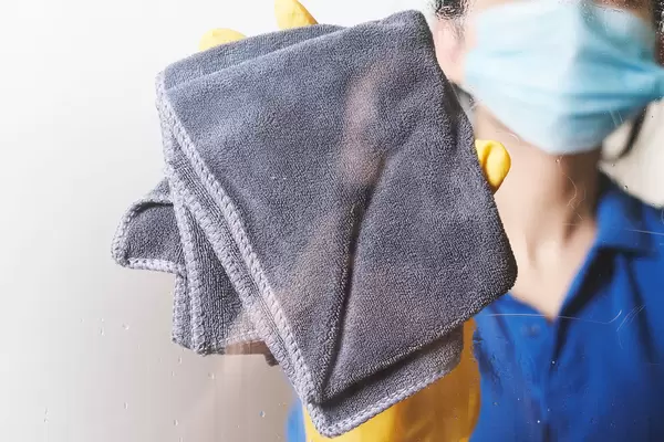 A housewife in face mask wiping window glass