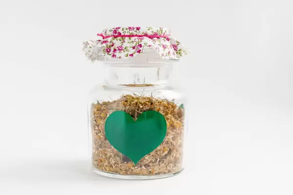 A jar of chamomile and herbs on white background