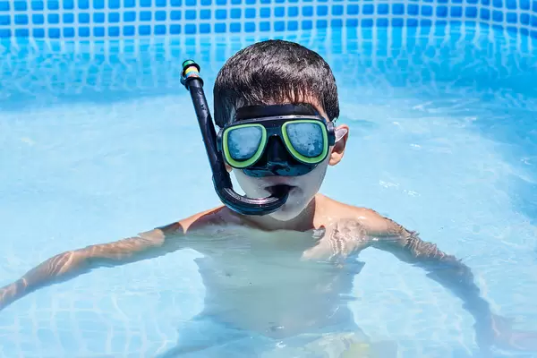 A kid boy of school age wearing mask and snorkel while diving in the pool during summer vacations