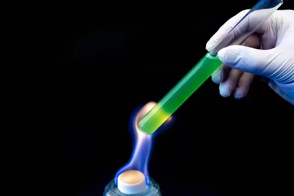 A laboratory test tube with a green solution in a man's hand is heated over a fire (Flip 2020)