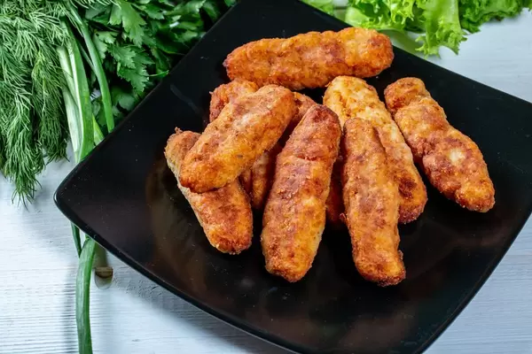 A lot of fish fingers on a black plate with greens in the background