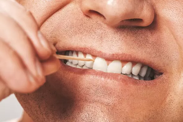 A man cleans his teeth using a wooden toothpick (Flip 2019)