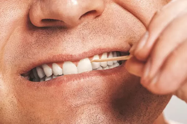 A man cleans his teeth using a wooden toothpick