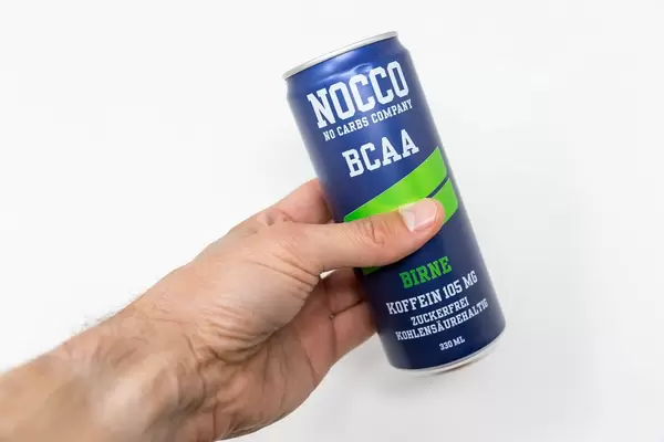 A man holds a can of NOCCO BCAA in the hand on a white background. This fitness drink, here in pear flavour, contains Branched Chain Amino Acid, L-carnitine, caffeine and six different vitamins