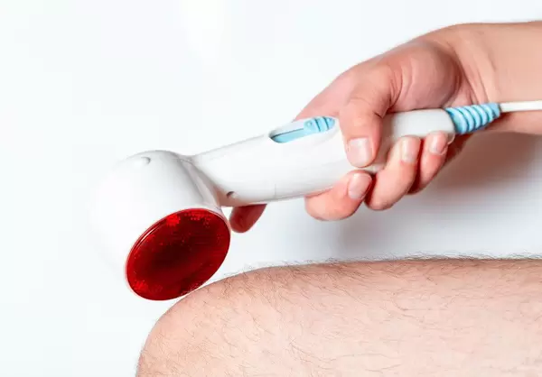 A man holds a heating and massage apparatus near his knee