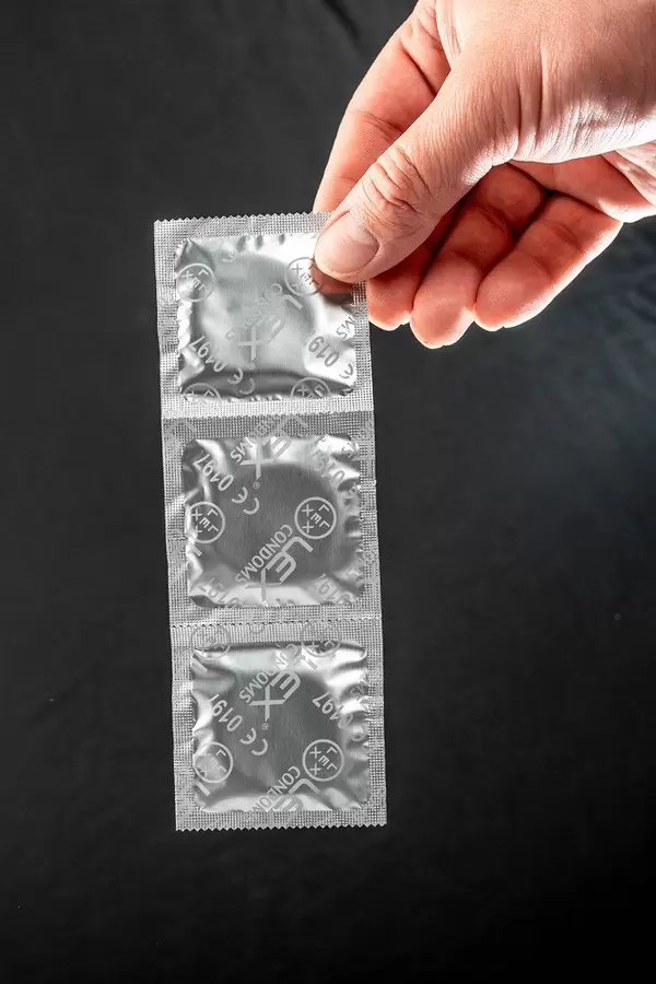 A man holds a pack of condoms on a black background