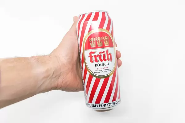 A man holds a red-white can of Früh Kölsch in his hand on a white background. Früh has over 110 years' history as traditional beer from Cologne, Germany